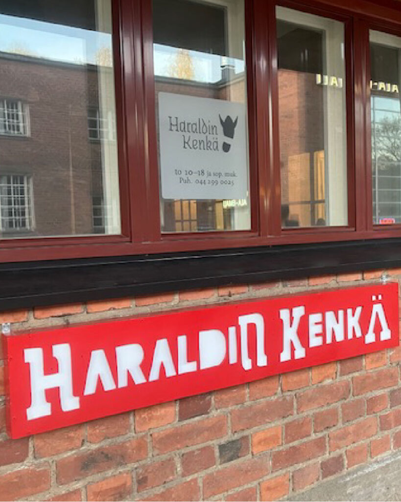 Ikkunoita, joiden alla tiiliseinää ja punainen kyltti, jossa lukee Haraldin Kenkä.