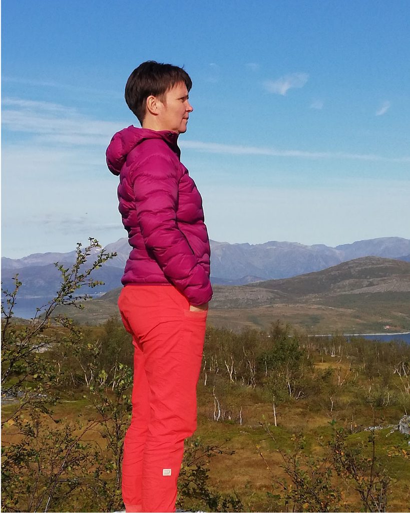 Nainen katsoo ulkona kaukaisuuteen taustallaan tuntureita ja sinistä taivasta.